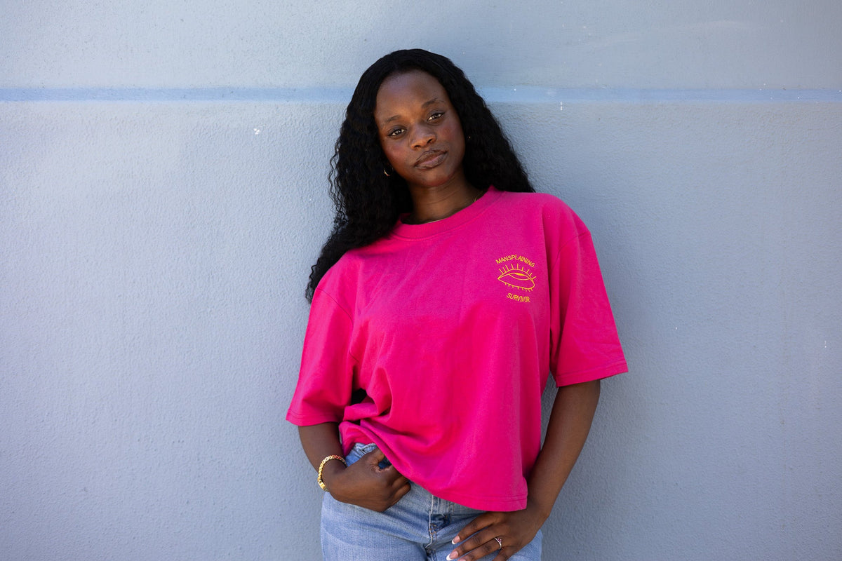 Woman leaning against a wall in the hot pink Mansplaining Survivor tee and jeans