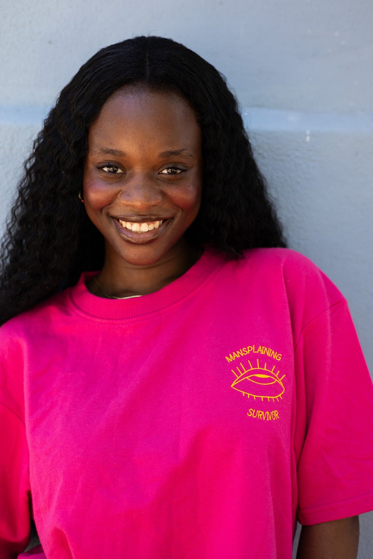 Smiling woman in the hot pink Mansplaining Survivor tee with orange embroidery