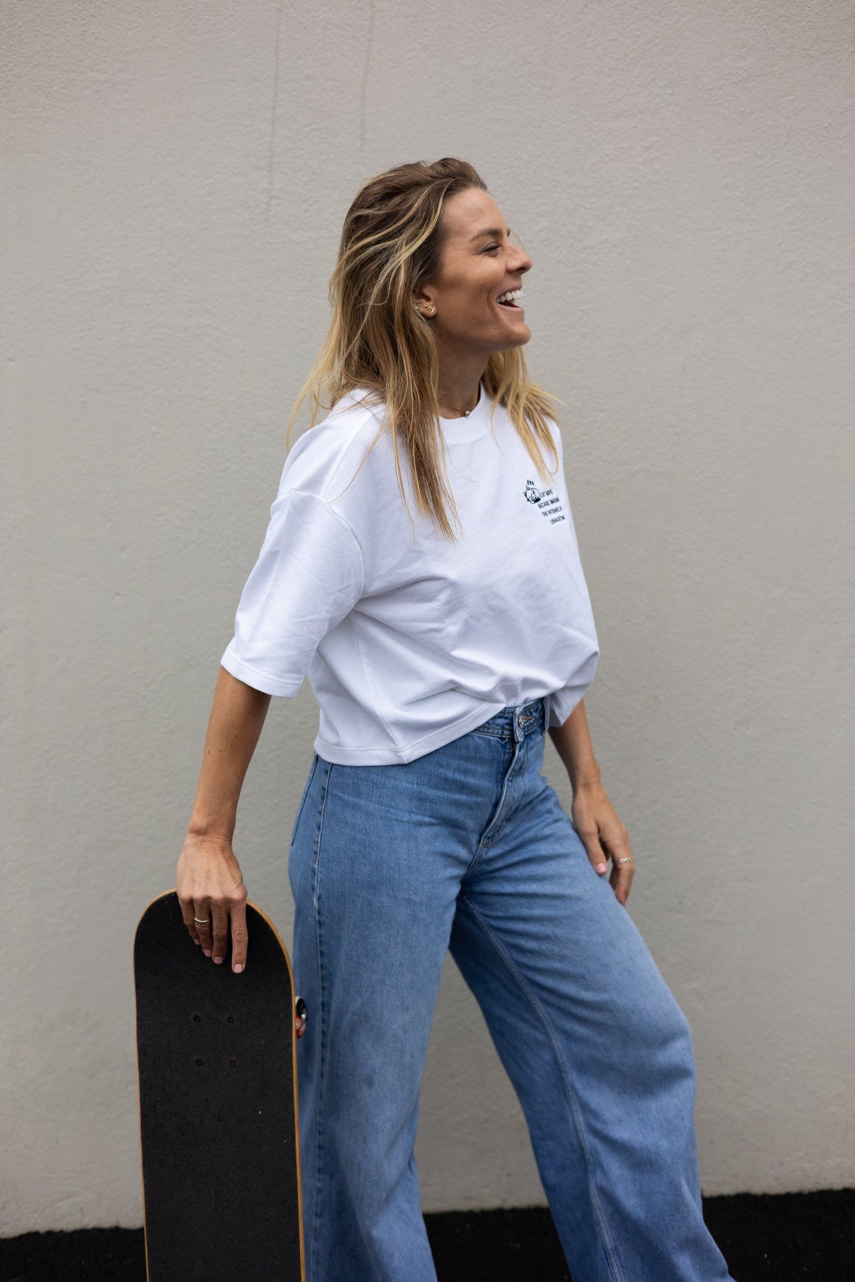 Side view of the white Cat Naps Because Smashing the Patriarchy is Exhausting tee worn with jeans and a skateboard