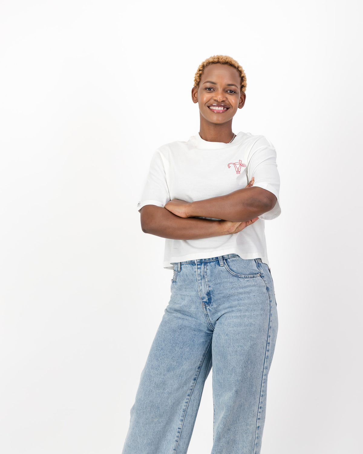 Smiling woman with her arms crossed in the white Uterus Zap tee and light blue jeans