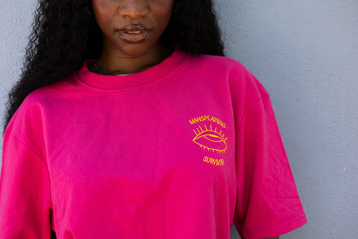 Close up of the orange Mansplaining Survivor embroidery on the hot pink tee