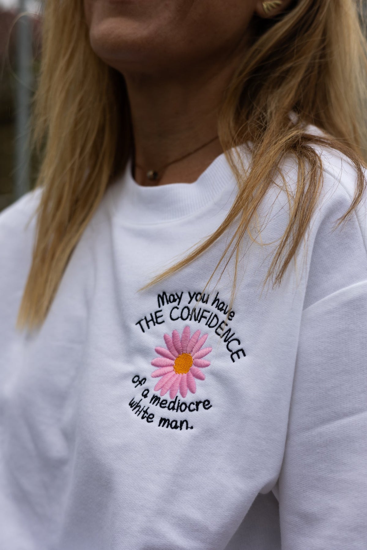Close up of the pink daisy embroidery reading May you have the confidence of a mediocre white man