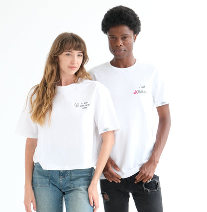 Two people in white WOMXN tees, the woman on the left wearing I'll Smile When You're Funny