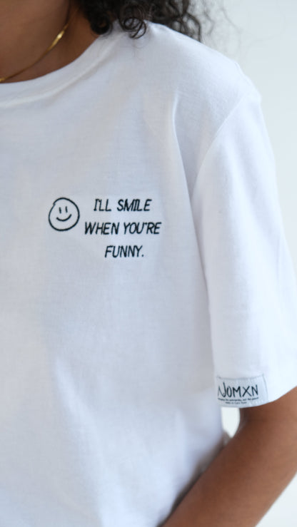 Close up of the smiley face embroidery and WOMXN sleeve label on the white I'll Smile When You're Funny tee