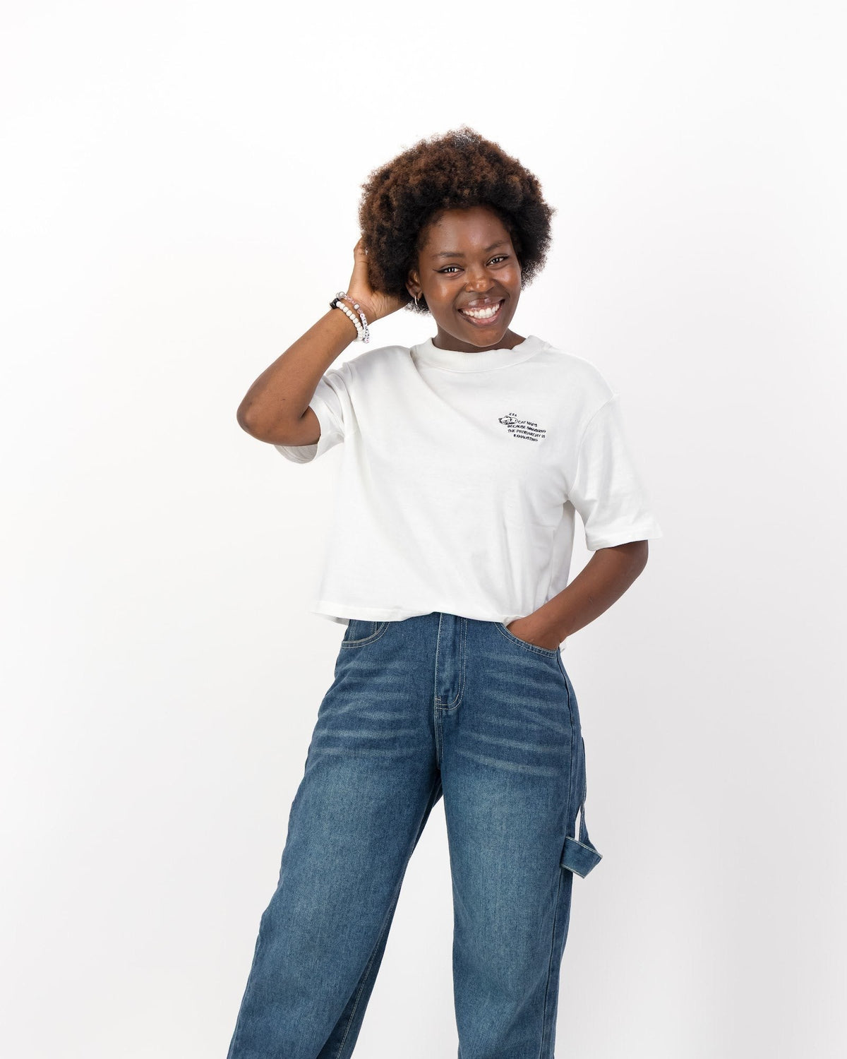 Smiling woman with one hand in her hair wearing the white Cat Naps Because Smashing the Patriarchy is Exhausting tee and jeans