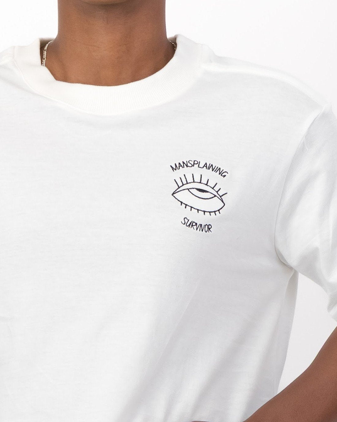 Close up of the black embroidered eye and Mansplaining Survivor slogan on the white tee
