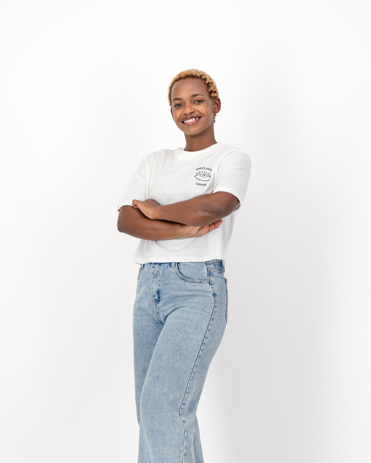 Smiling woman with her arms crossed in the white Mansplaining Survivor tee and jeans