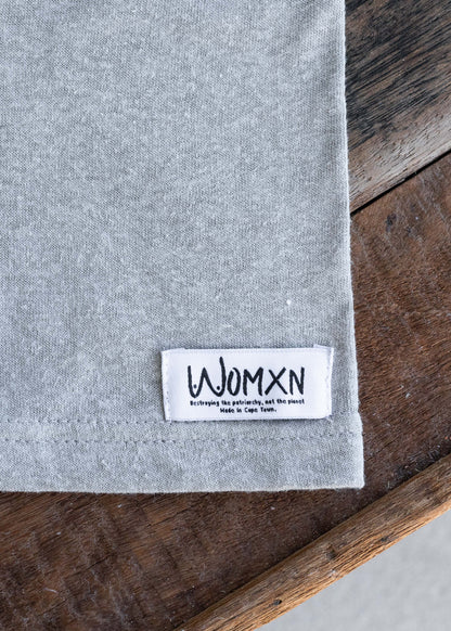 Close up of the woven WOMXN label on the hem of the grey Too Clumsy to be Around Fragile Masculinity tee