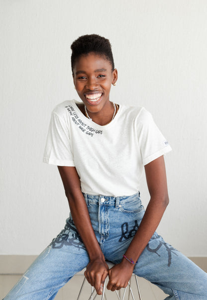 Smiling woman sitting on a stool in the white Care Less About Thigh Gaps and More About Wage Gaps tee and jeans