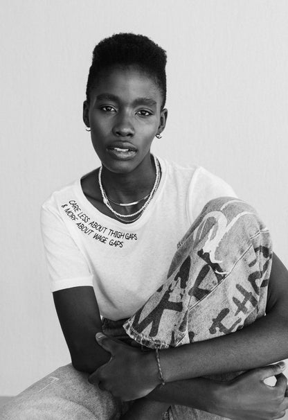 Black and white photo of a woman holding a bag, wearing the Care Less About Thigh Gaps and More About Wage Gaps tee