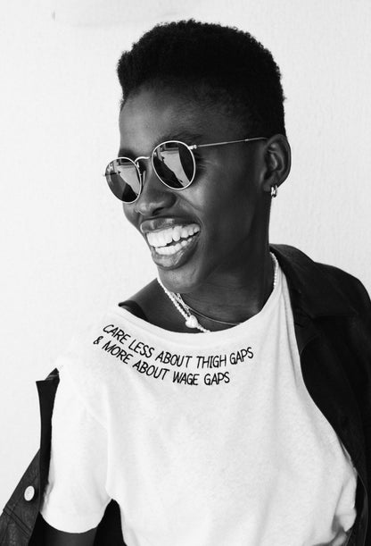 Black and white photo of a laughing woman in sunglasses wearing the Care Less About Thigh Gaps and More About Wage Gaps tee