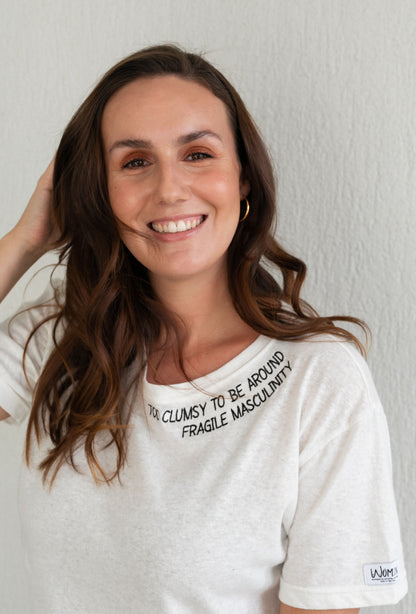 Smiling woman with a hand in her hair wearing the white Too Clumsy to be Around Fragile Masculinity tee
