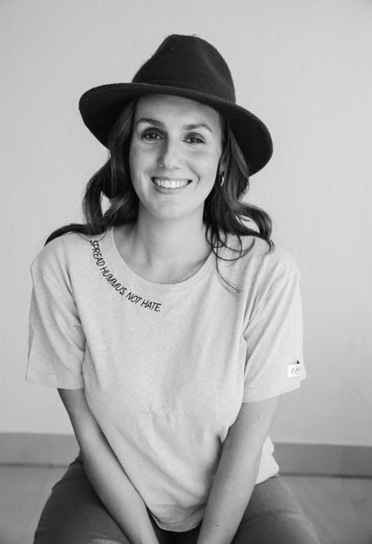 Black and white photo of a smiling woman in a hat wearing the Spread Hummus Not Hate tee